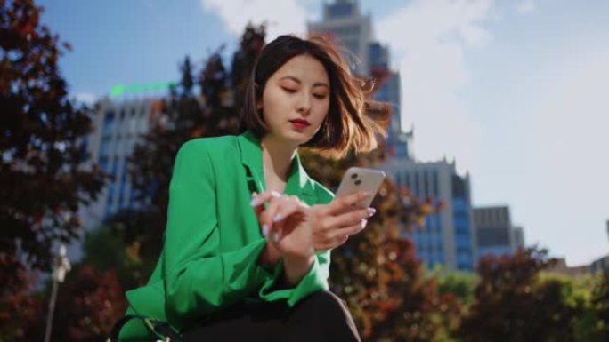 在市中心的公园区用现代智能手机描绘了迷人的中国女人的肖像，富有而成功
