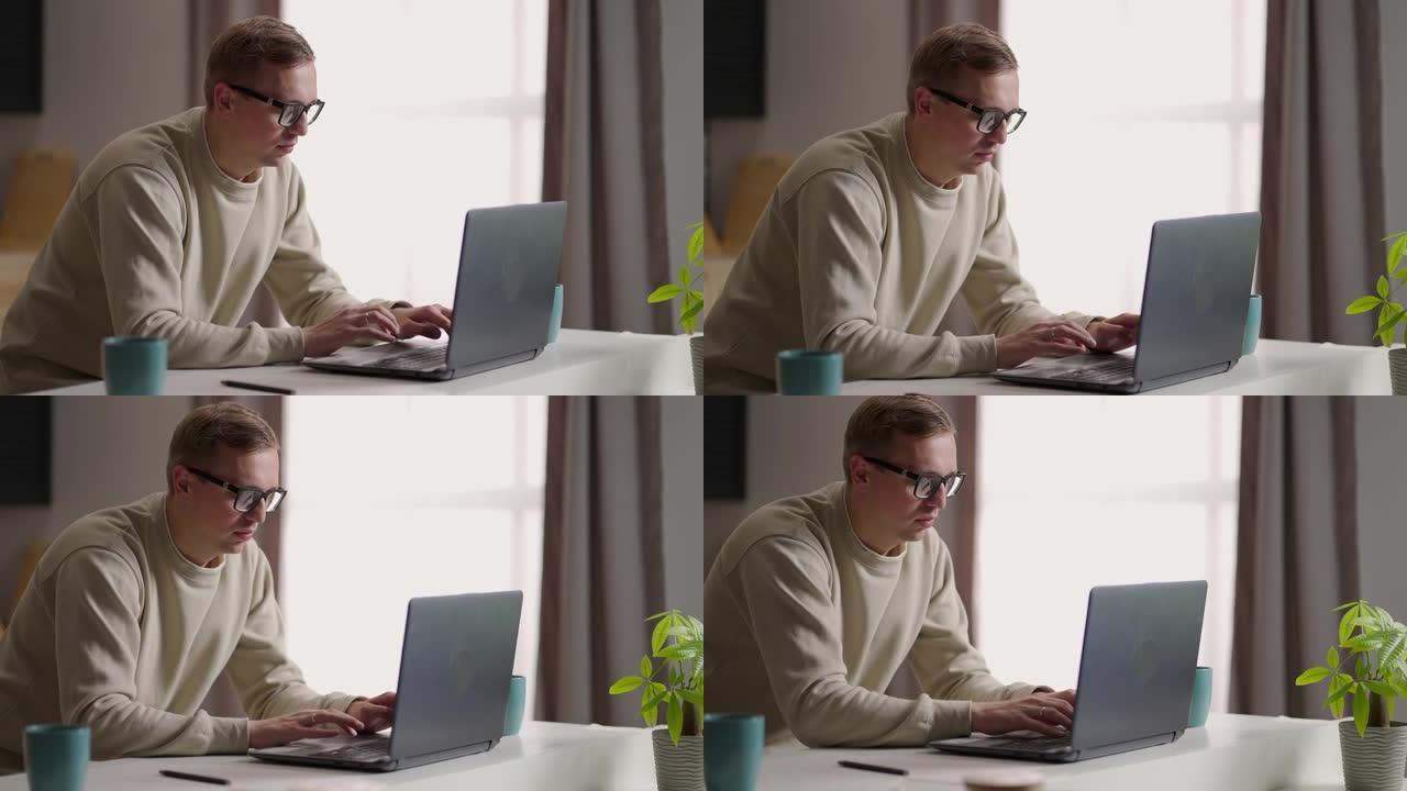 一名戴眼镜的男子在家中使用笔记本电脑和互联网在厨房工作。远程工作和远程学习