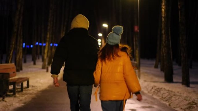在寒冷的冬季街道上奔跑的快乐年轻夫妇的跟踪镜头。后视图快乐兴奋的有爱心的男人和女人在城市享受夜间休闲