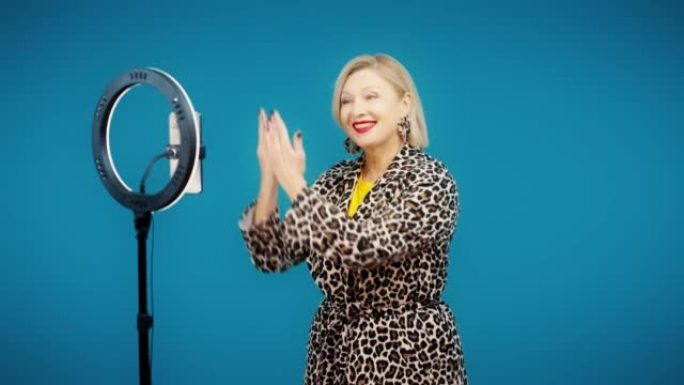 穿着时髦外套的快乐高级女人在手机摄像头上跳舞，受欢迎的博客作者