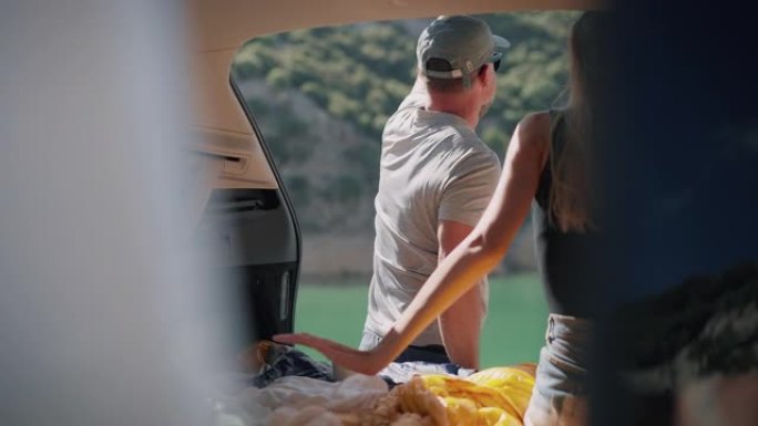 一对情侣坐在美丽的绿松石湖边的汽车后备箱里