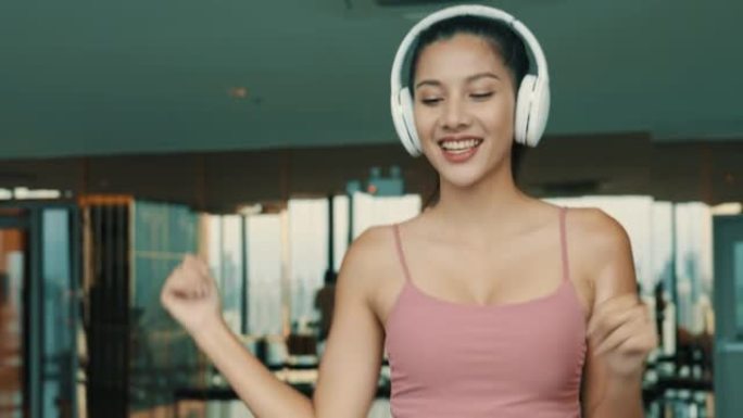 美女运动员在带耳机的跑步机上散步时跳舞
