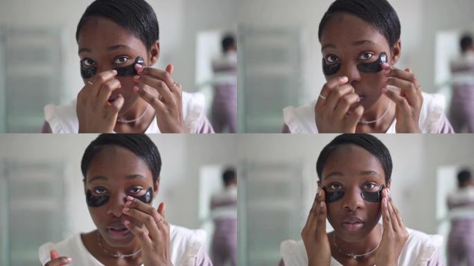 年轻的非洲裔美国集中妇女在慢动作中使用眼罩的特写脸看着相机。早上在浴室照顾皮肤的苗条美丽女士的前视图