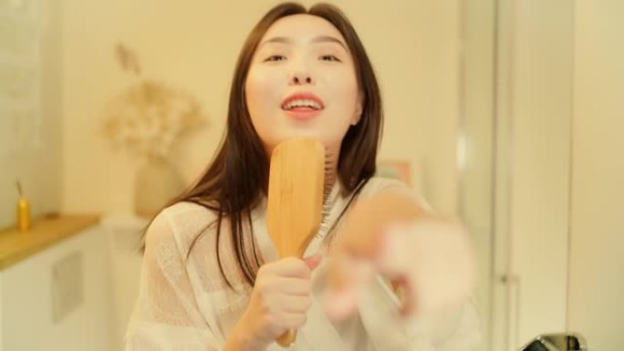 感觉棒极了。亚洲女性享受早上的浴室活动，在镜子前玩得开心。对着发刷唱歌，用力跳舞
