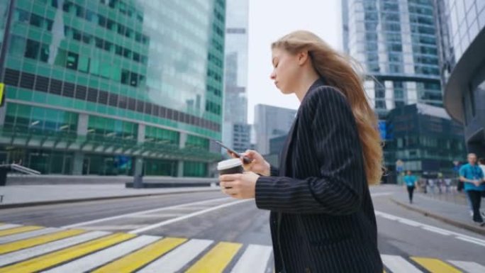 一位女商人走在城市的人行横道上，查看智能手机上的通知