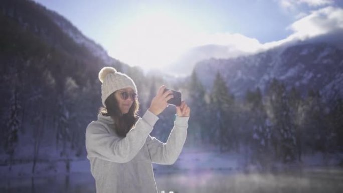 年轻女子在白雪皑皑的湖边用手机拍照