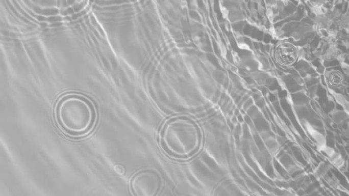 透明清晰的平静水面纹理，带有波浪、飞溅和气泡。时尚抽象自然背景。白灰色的水在阳光下波动。慢动作全高清