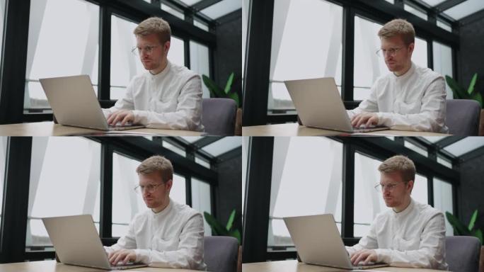 戴眼镜的成年男子正在办公室或同事中使用笔记本电脑，键入消息或报告