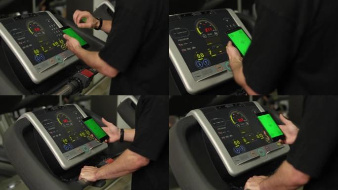 无法识别的男人在健身房的跑步机上行走时使用带有绿屏的智能手机