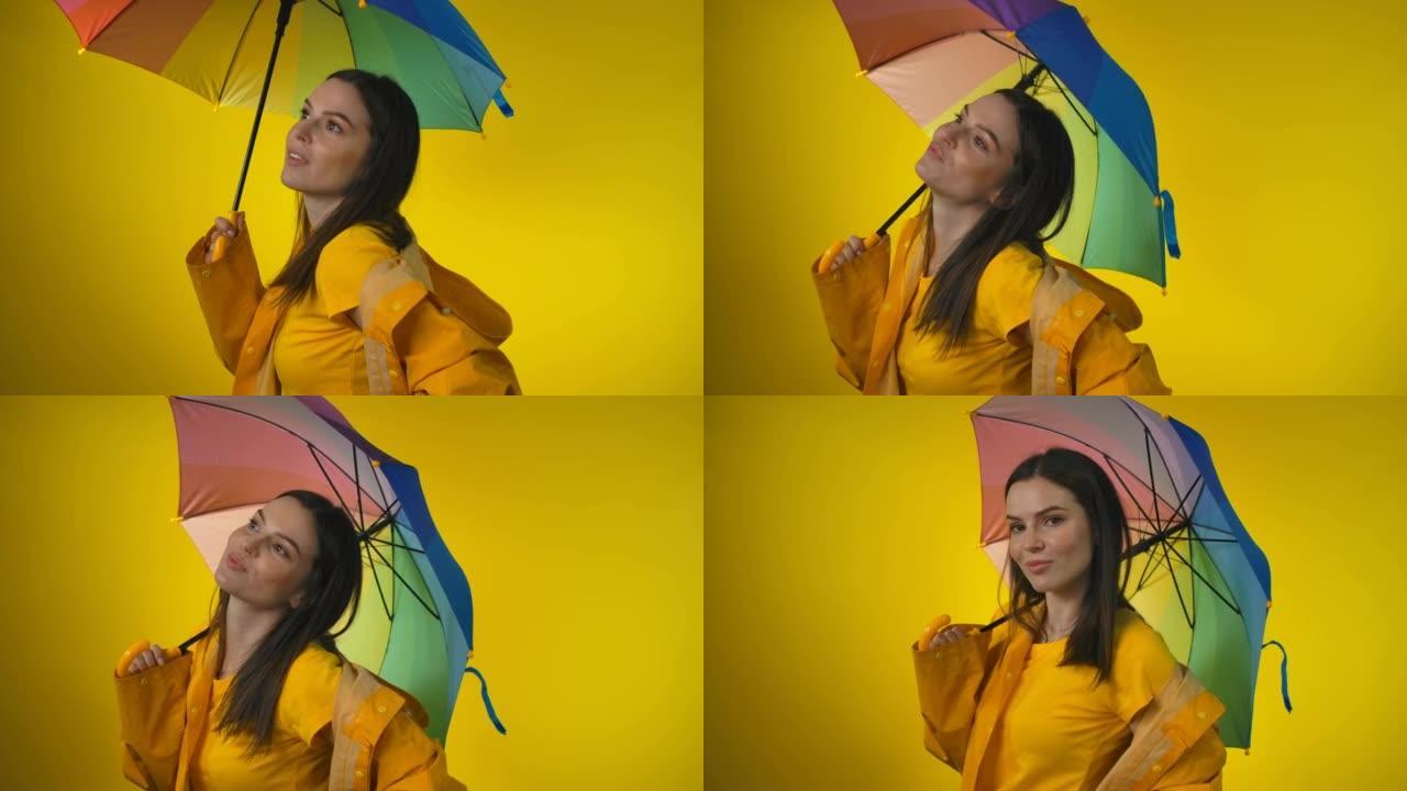 穿着黄色雨衣的开朗女人打着彩虹伞正在检查雨水