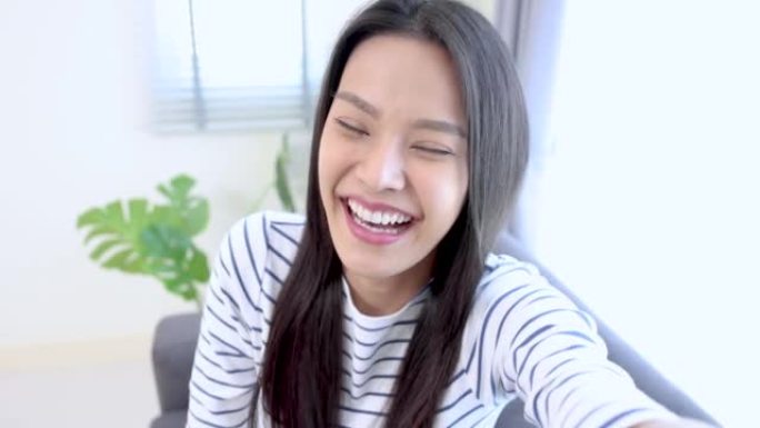 美丽的亚洲女人看着相机微笑，在家里的客厅快乐，视频通话。