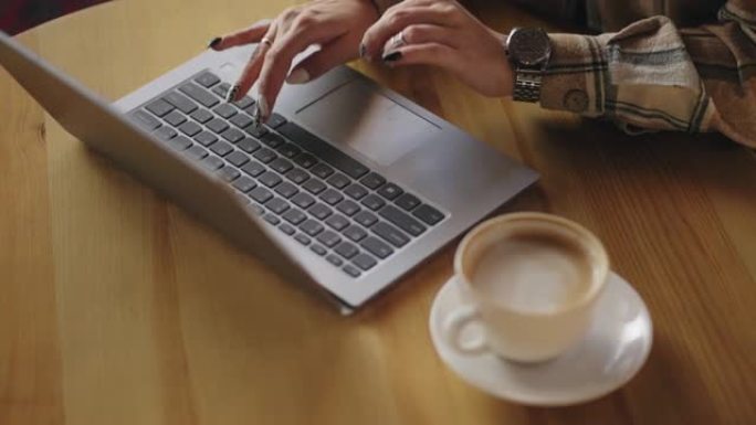 自由职业者的女人正在咖啡馆使用笔记本电脑，键盘和咖啡杯上的手的特写视图