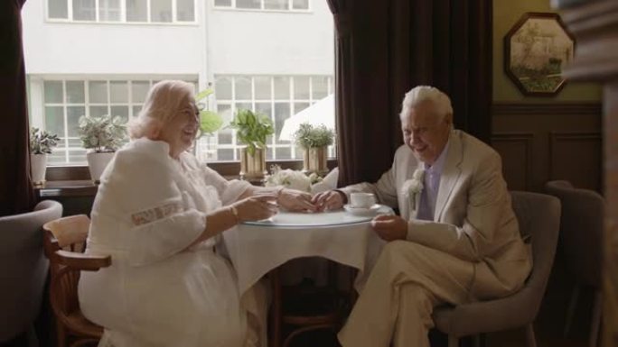 一对老年夫妇坐在咖啡馆里的桌子旁笑着。
