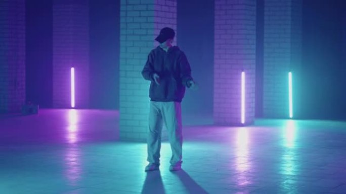 一个钢铁人在带有紫色蓝色霓虹灯的大厅中以现代风格跳舞嘻哈自由泳。男性职业嘻哈舞者