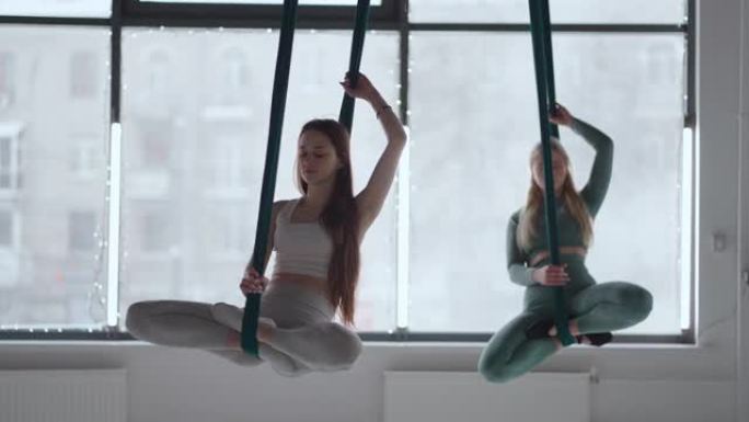 两名年轻女子在吊床上摇摆，冥想专注于呼吸。航空瑜伽
