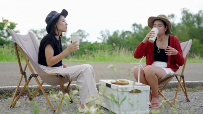 亚洲女孩坐在野营椅上，吃喝，在与大自然放松的一天放松。