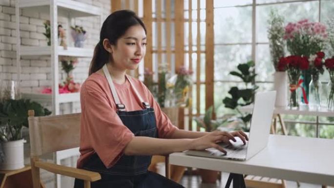 穿着围裙的亚洲妇女使用笔记本电脑工作