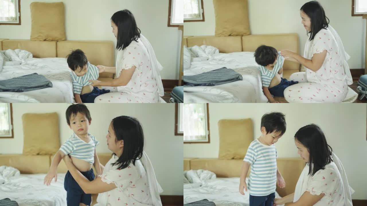快乐的亚洲妈妈在家洗澡前给学龄前儿子脱衣服。