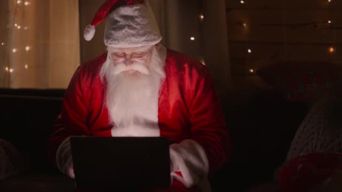肖像: 在笔记本电脑上工作的圣诞老人通过电子邮件发送或接收圣诞节或新年的祝福或祝贺信。
