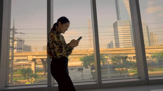 亚洲女商人晚上在市中心的办公室大厅里散步和使用手机。