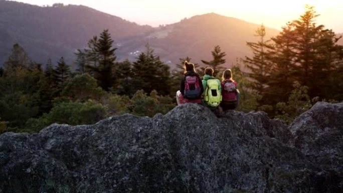 空中无人机拍摄的三名山地自行车手坐在日落时休息的岩石山脊上