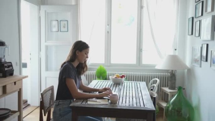 年轻女子坐在桌子旁的笔记本电脑上打字