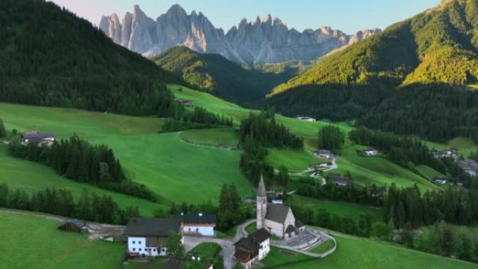 在意大利圣马格达莱纳的多洛米蒂阿尔卑斯山的一座教堂和山脉的空中无人机日出视图。