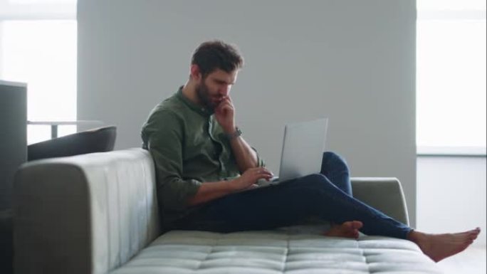 年轻人周末在家用现代笔记本电脑上网，人坐在沙发上