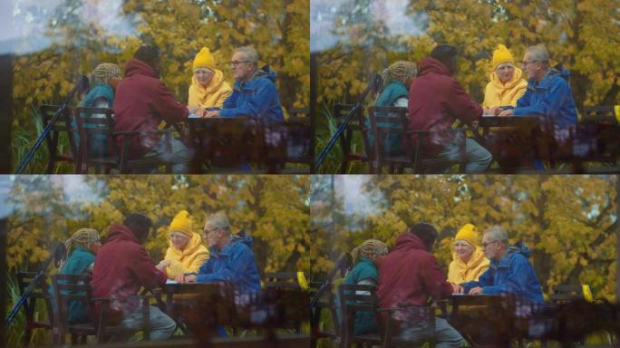 老年夫妇和非洲族裔青少年北欧散步休息，在公园餐桌上喝茶。从室内观看