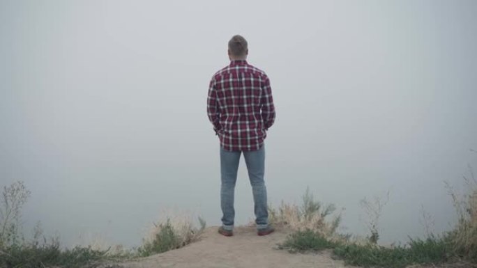年轻的高加索自信男子站在悬崖上眺望别处。实时摄像机放大到户外享受大自然美景的人。孤独和生活方式概念。