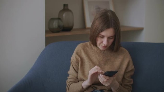 女商人在家庭办公室用手机打字信息。年轻女孩在电话里慢动作聊天。在沙发上使用智能手机关闭年轻女性的手。