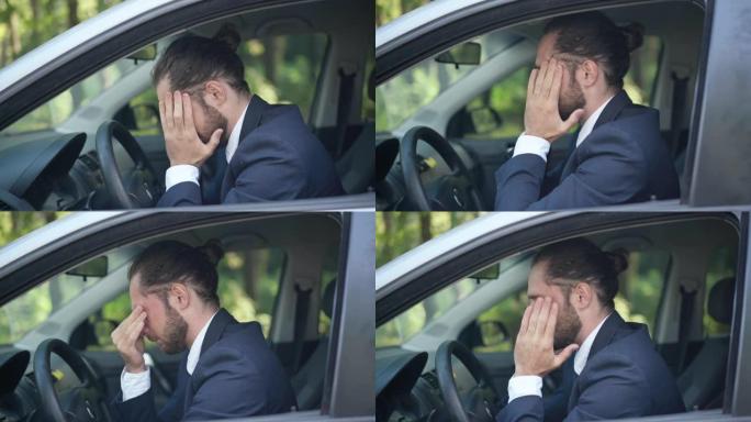 年轻紧张的白人男子坐在驾驶座上摩擦太阳穴叹息的侧视肖像。满目疮痍的英俊大胡子商人在户外的车里思考。问