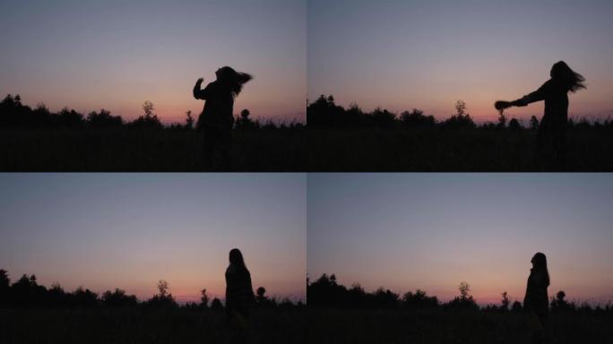 20岁快乐年轻女子的剪影在美丽的日落前举起双臂。白人女性站在田野里看着惊人的日出。徒步旅行女孩享受平