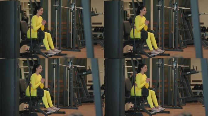 强壮的西班牙裔女运动员在模拟器上做腿部稀释练习。穿着黄色运动服的运动健身房的黑发女人在腿部压榨机上锻