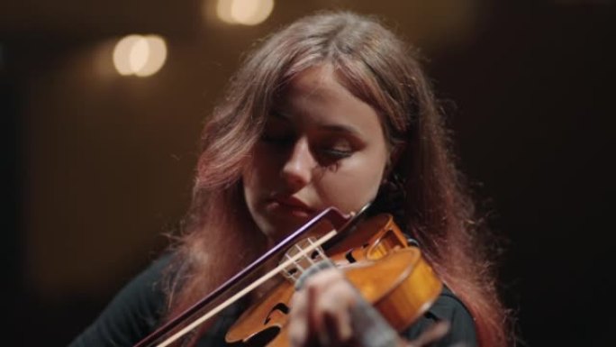 漂亮的年轻女子在音乐厅，肖像的现场在交响乐团中演奏小提琴