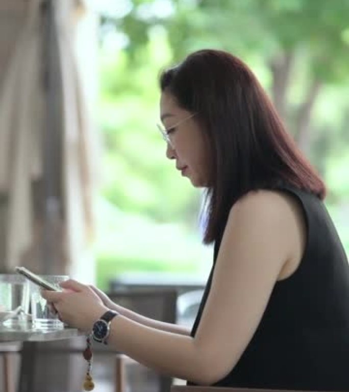 坐在咖啡店外面玩智能手机的亚洲妇女