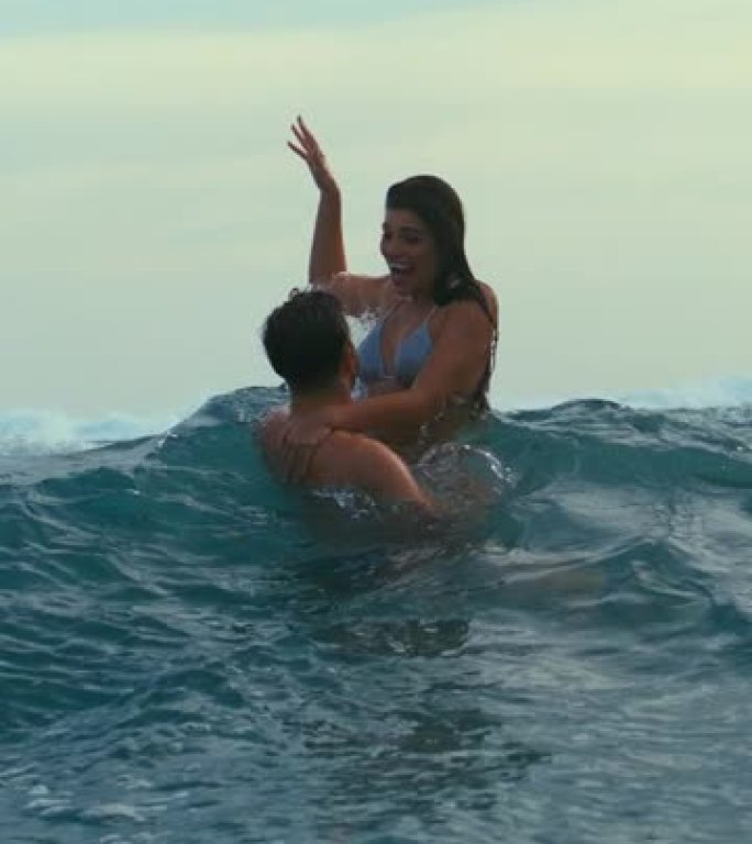 海滩上的浪漫情侣。在海中玩耍一起在海浪中游泳，拥抱垂直视频