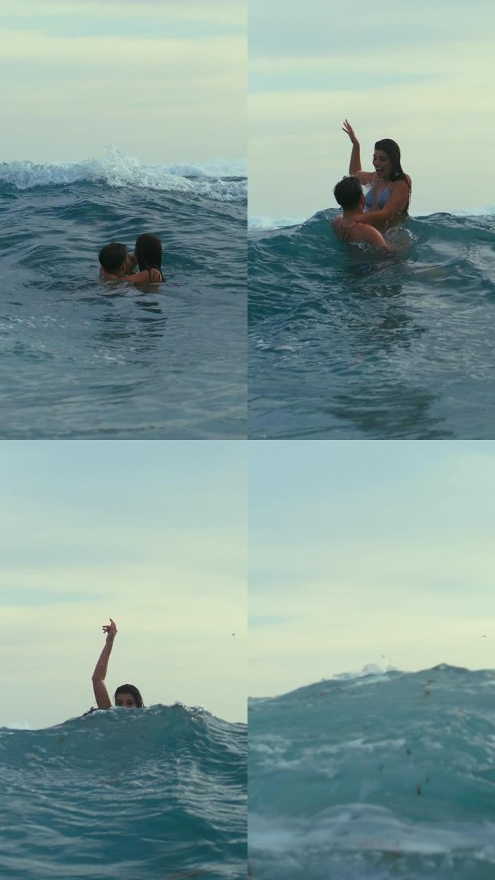 海滩上的浪漫情侣。在海中玩耍一起在海浪中游泳，拥抱垂直视频
