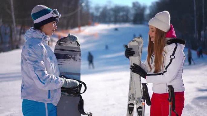侧视图两位自信的女性讨论不同冬季运动的优缺点。美丽苗条的年轻高加索千禧一代女士站在斜坡上白雪上做手势
