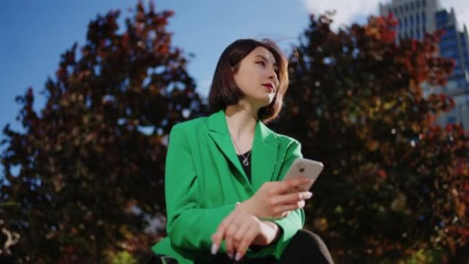 无忧无虑的中国妇女在市中心的公园里休息，使用智能手机，观看社交媒体