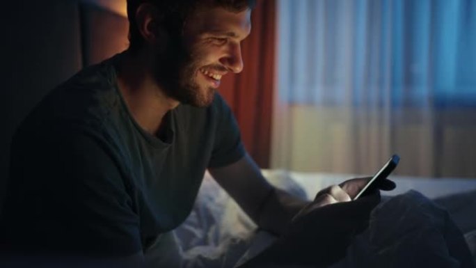 男人在睡觉前使用智能手机，坐在床上，肖像时沉迷于互联网和社交媒体
