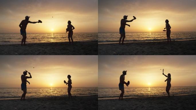 日落时在海滩上享受桨网球的男人和女人的剪影