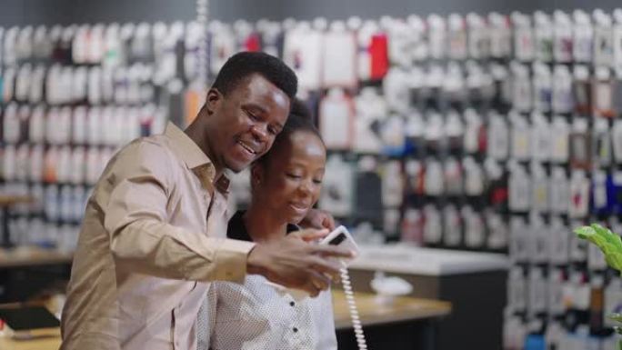 快乐的非洲裔美国夫妇在数字设备商店，购物者正在检查智能手机展览样本的相机，一起自拍