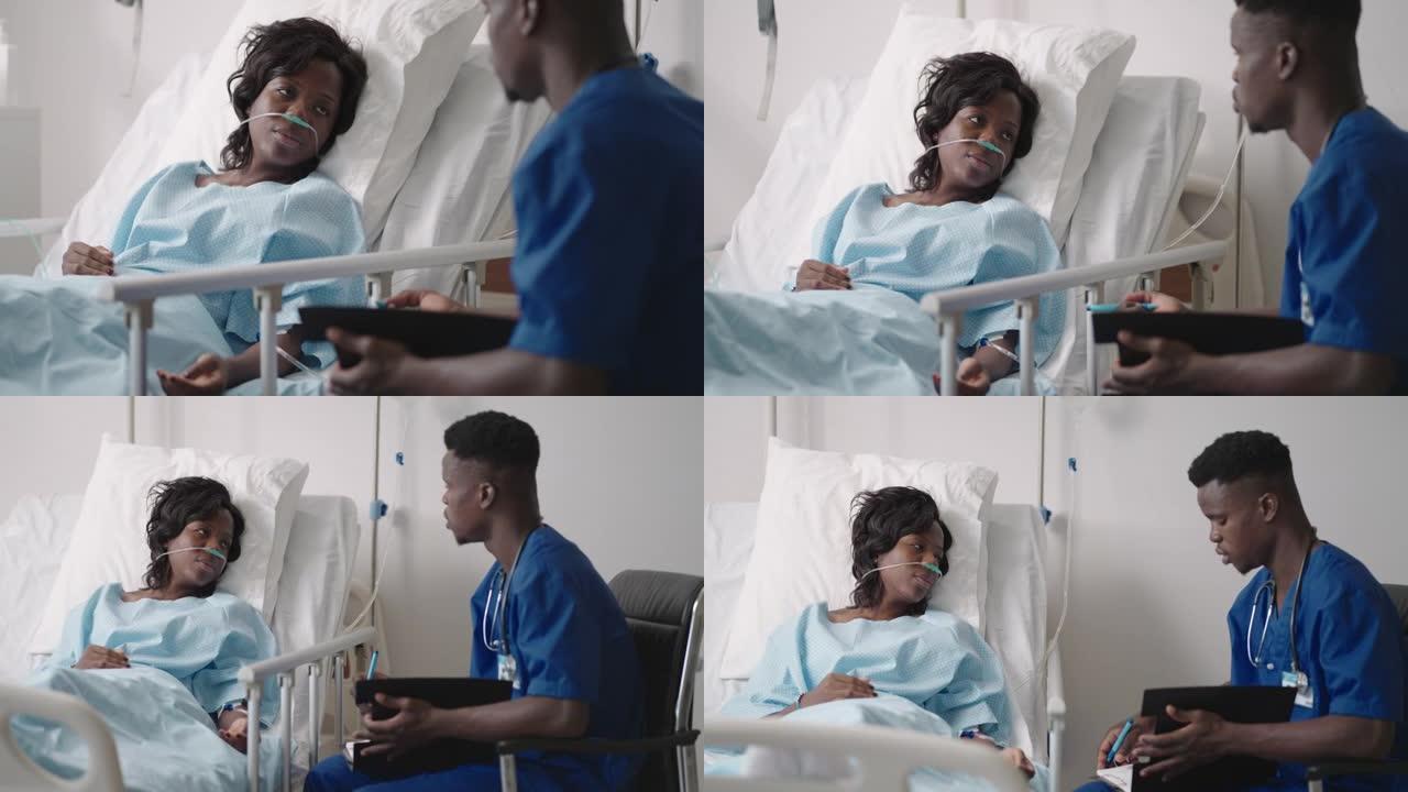 手术后在医院病床上休息的非裔美国妇女与年轻的男护士交谈。非裔美国护士协助躺在床上的女性患者的肖像