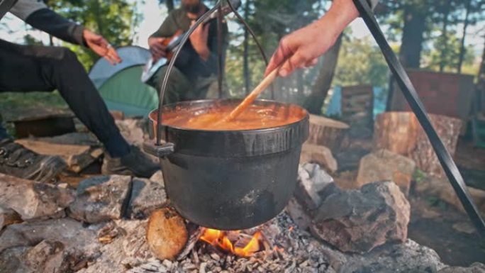 SLO MO Man在篝火上的铸铁锅中搅拌炖肉