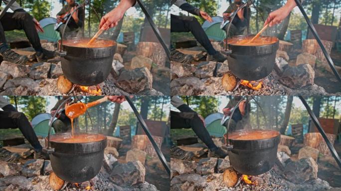 SLO MO Man在篝火上的铸铁锅中搅拌炖肉
