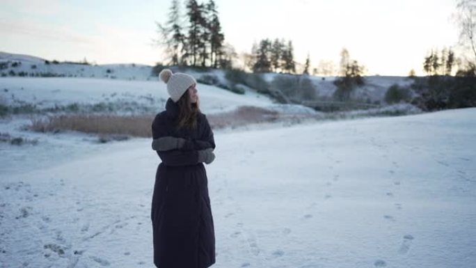 穿着冬季夹克的女人站在白雪皑皑的田野里，表现出寒冷的迹象