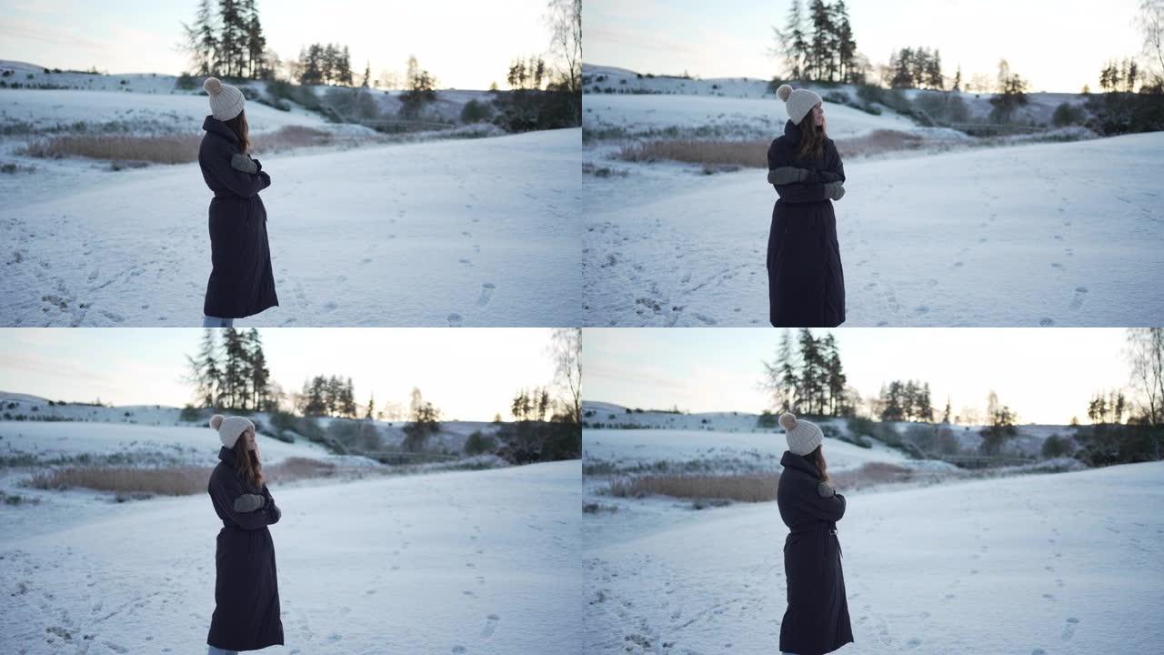 穿着冬季夹克的女人站在白雪皑皑的田野里，表现出寒冷的迹象