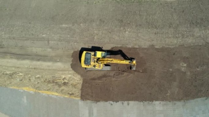 黄色挖掘机，带连续履带。鸟瞰图。高空摄像机。找平挖掘机。施工现场准备。装满挖掘机的铲斗。
