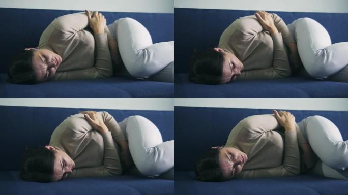 深陷心烦意乱的黑发女人躺在沙发上摸着肚子，感到难以忍受的胃痛，痛经，月经疼痛和腹部绞痛，流产，流产